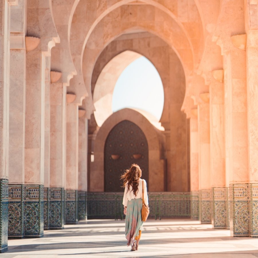 Mulher caminhando sob os arcos de mosaico de um pátio marroquino