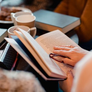 Mulher lendo um livro sobre a mesa, ao lado de xícaras de café